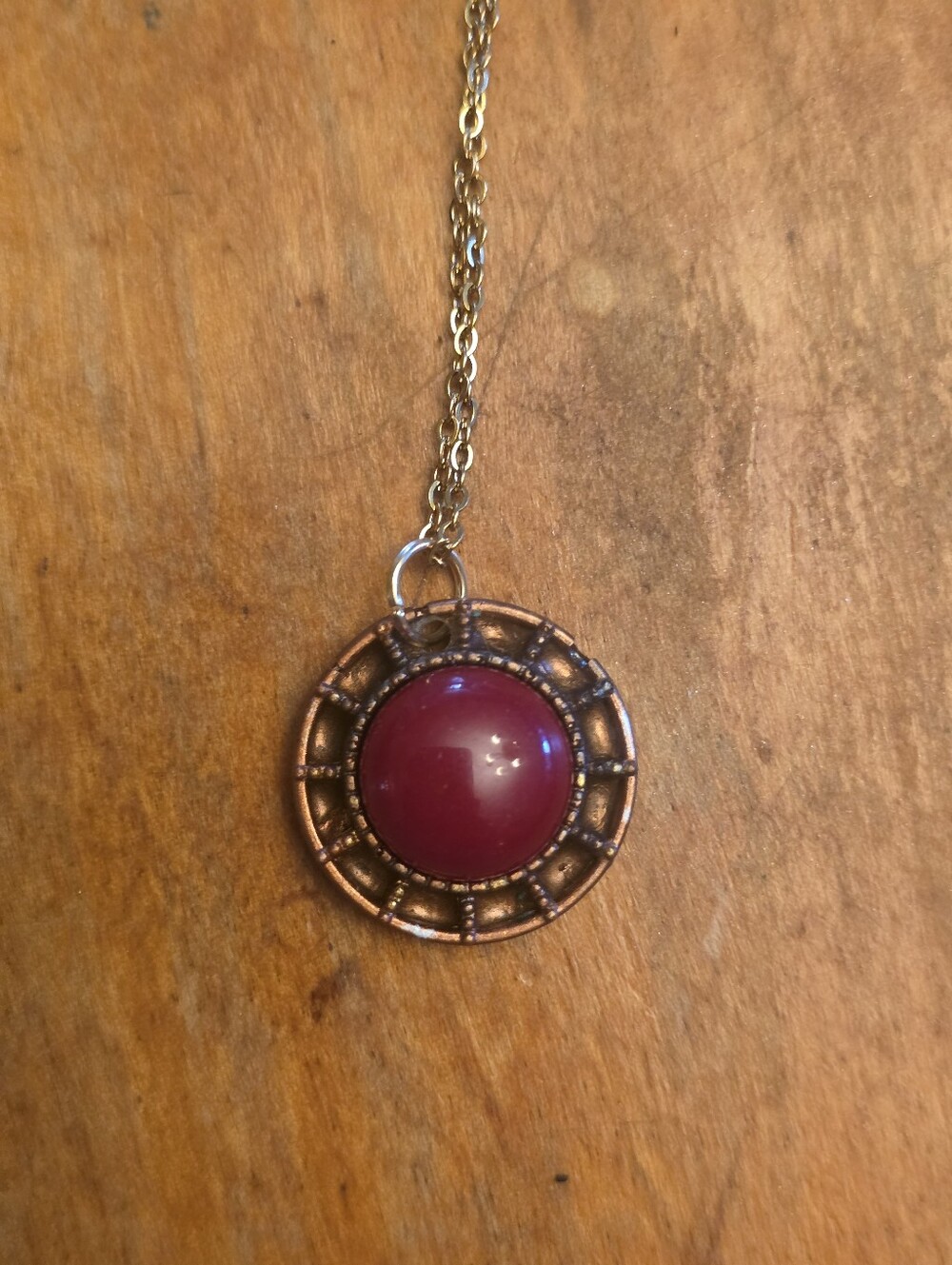 Small Red Gemstone Inside A Tan Resin Frame On A Gold Tone Chain Necklace